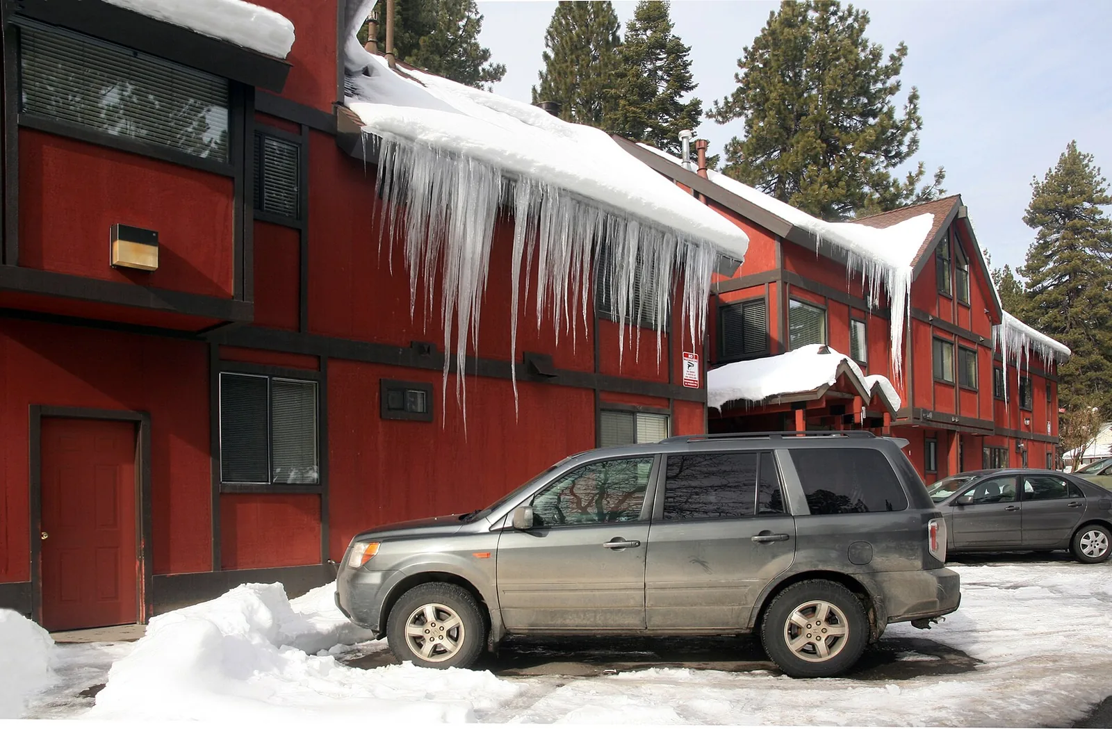 Long icicles hanging from the snow-covered roof of a red two-story motel in South Lake Tahoe, California, with an SUV parked in the cleared lot
