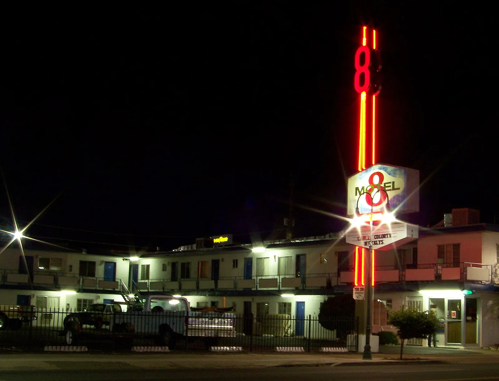 A two-story motel at night with a tall lit sign and a marquee advertising weekly rates, with pickup trucks parked in the lot