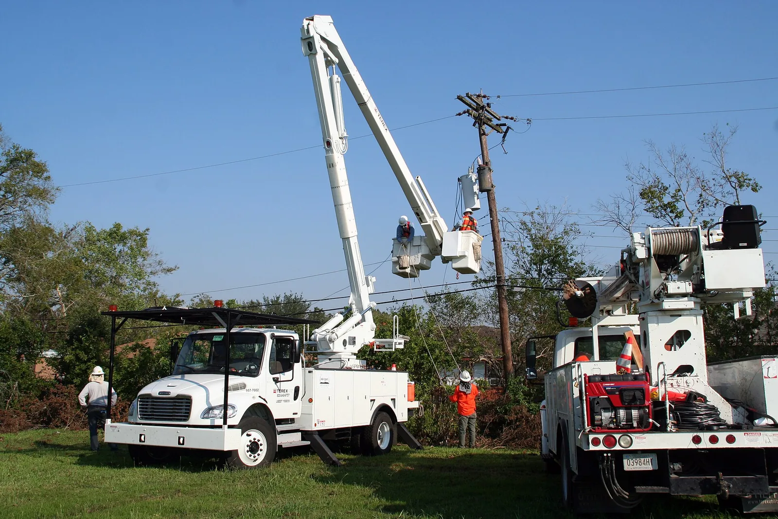 Two white bucket trucks with line workers in the buckets repairing a power pole in Houston, Texas, in September 2008