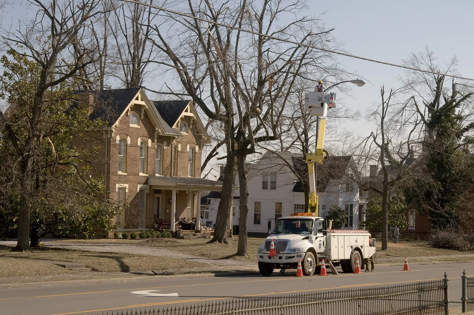 A utility bucket truck repairing a street light on a tree-lined street of brick houses in Madisonville, Kentucky, in February 2009